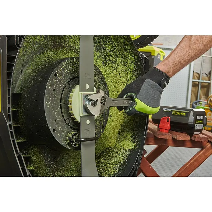 Ryobi Max Power Akku-Rasenmäher RY36LMXSP46A-150 - 36 V, 1 Akku, 5 Ah, Schnittbreite: 46 cm - Ein Mann wechselt mit einem Schraubenschlüssel die Klinge eines Rasenmähers von Ryobi, wobei ein Akku der Marke Max Power in der Nähe liegt.