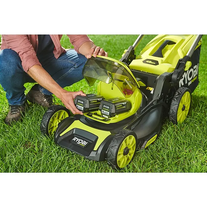 Ryobi Max Power Akku-Rasenmäher RY36LMXSP46A-150 - 36 V, 1 Akku, 5 Ah, Schnittbreite: 46 cm - Nahaufnahme eines Mannes, der zwei RYOBI MAXPOWER-Akkus in einen Rasenmäher einsetzt, der auf einem grünen Rasen steht.