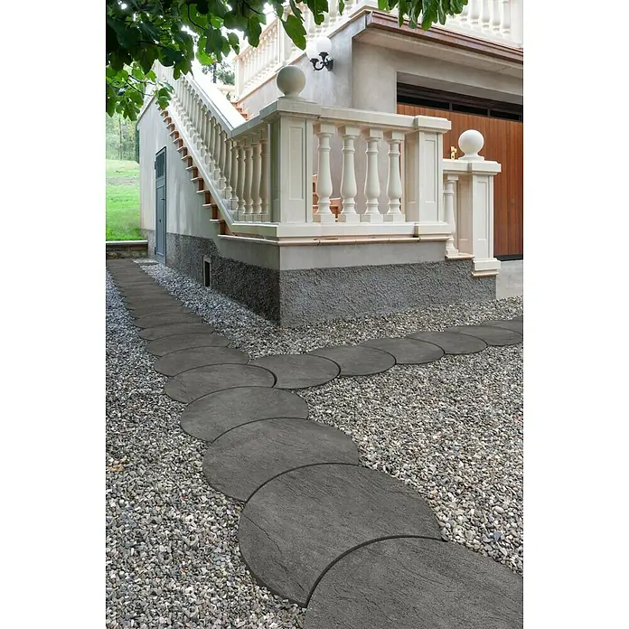 SAS Trittstein Luna - 34 x 47 x 3 cm, Anthrazit, Beton - Kreisförmiger Gehweg aus Betonplatten im Garten. Die grauen Steine bilden einen Pfad durch den Kies, der zum Haus führt.