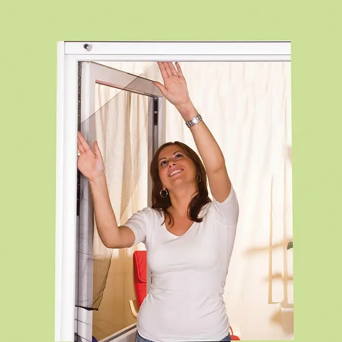 Easy Life Sonnen-& Insektenschutz-Gitter - B x H: 130 x 150 cm, Montage Insektengitter: Ankletten - Eine Frau installiert ein Fliegengitter an einer Tür, um Insekten fernzuhalten und frische Luft hereinzulassen.