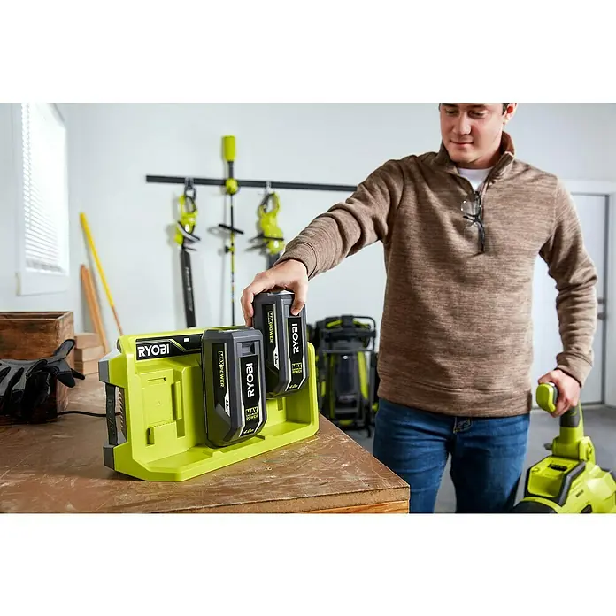 Ryobi Max Power Batterie-Ladegerät 3-fach RY36C3PA - Passend für: Ryobi 36V Akkus - Ein Mann platziert einen Ryobi Max Power Akku in eine grüne Ryobi Ladestation, die auf einer Werkbank steht. Im Hintergrund Gartengeräte.