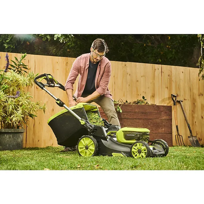 Ryobi Max Power Akku-Rasenmäher RY36LMXSP46A-150 - 36 V, 1 Akku, 5 Ah, Schnittbreite: 46 cm - Ein Mann leert einen Ryobi Rasenmäher-Fangkorb auf einem gepflegten Rasen vor einem Holzzaun, der die Funktionalität hervorhebt.