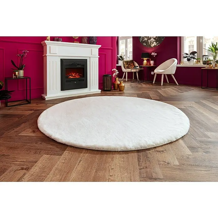 Fellteppich Happy - Elfenbein, Durchmesser: 160 cm, 100 % Polyester (Flor) - Weißer, runder Teppich aus Kunstfell auf einem Holzboden vor einem Kamin, der eine warme und gemütliche Atmosphäre im Raum schafft.
