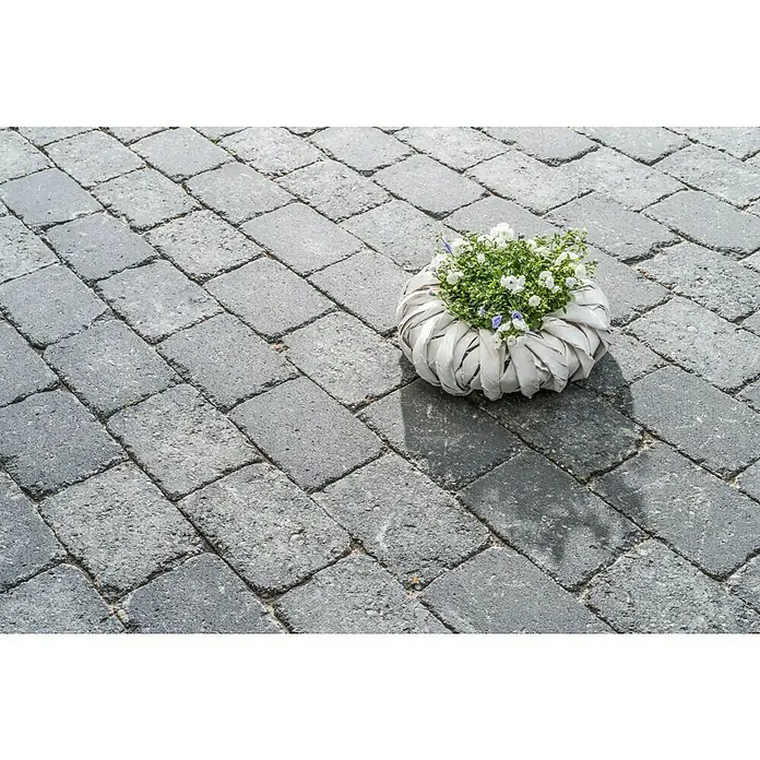 Diephaus Pflasterstein Austin - Basalt, 21 x 14 x 7 cm, Rechteckig - Nahaufnahme eines Blumenarrangements in einem weißen, gewebten Behälter auf einem gepflasterten Weg.