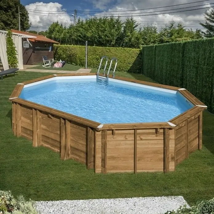 Gre Piscina de madera Avocado - L x An x Al: 656 x 456 x 131 cm, Natural, 24.700 l - Una piscina octogonal de madera en el jardín, llena de agua azul y clara, rodeada de césped cuidado y setos verdes.