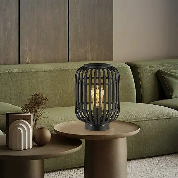 Home Sweet Home Bamboo Tischleuchte - 10 W, L x B x H: 21,5 x 21,5 x 30 cm, Schwarz, E27 - Schwarze Tischlampe mit Käfigdesign und Edison-Glühbirne auf einem Beistelltisch neben einem grünen Sofa im Wohnzimmer.