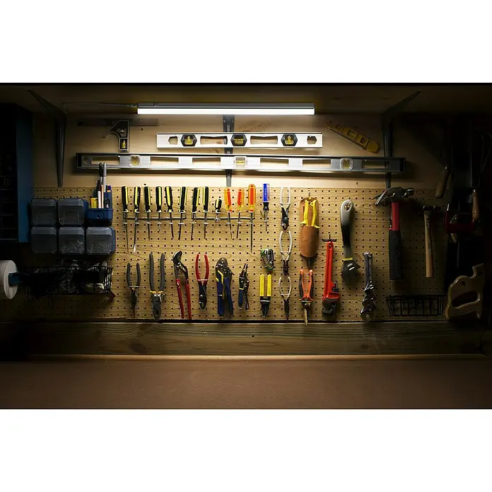 Ledvance LED-Unterbauleuchte Batten SensorLänge: 57,3 cm, Warmweiß - Ordnungssystem: Werkzeuge wie Schraubenzieher und Zangen hängen an einer Werkzeugwand über einer Arbeitsfläche, beleuchtet von einer Lampe.