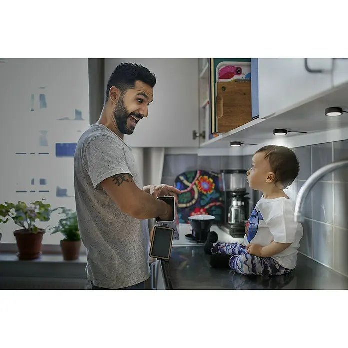 Ledvance LED-Unterbauleuchten-Set Spot Puck - Warmweiß, Schwarz - Der Vater zeigt seinem Kind eine moderne, tragbare Kaffeemaschine in der Küche. Die Kaffeemaschine ist kompakt und leicht zu transportieren.