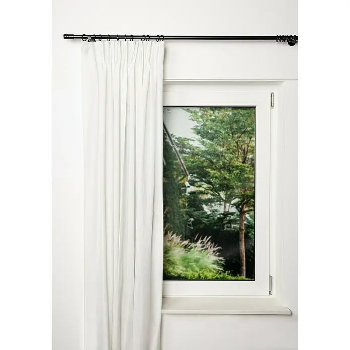 Expo Ambiente Stilgarnitur Rillcube - Länge Gardinenstange: 210 cm - 400 cm, Schwarz - Weißer Vorhang hängt an einer schwarzen Gardinenstange vor einem Fenster mit Blick auf Bäume.