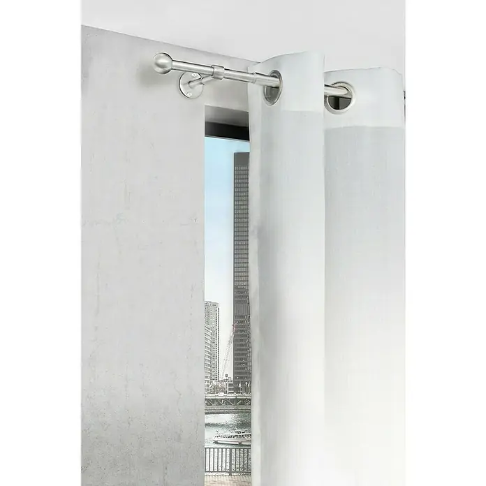 Komplettgarnitur 2in1 - Edelstahloptik, 160 cm - 280 cm, Metall, Ausziehbar - Weisse Gardinenstange mit Metallösen vor einem Fenster mit Stadtblick. Die Stange ist aus silbernem Metall und hat runde Endstücke.