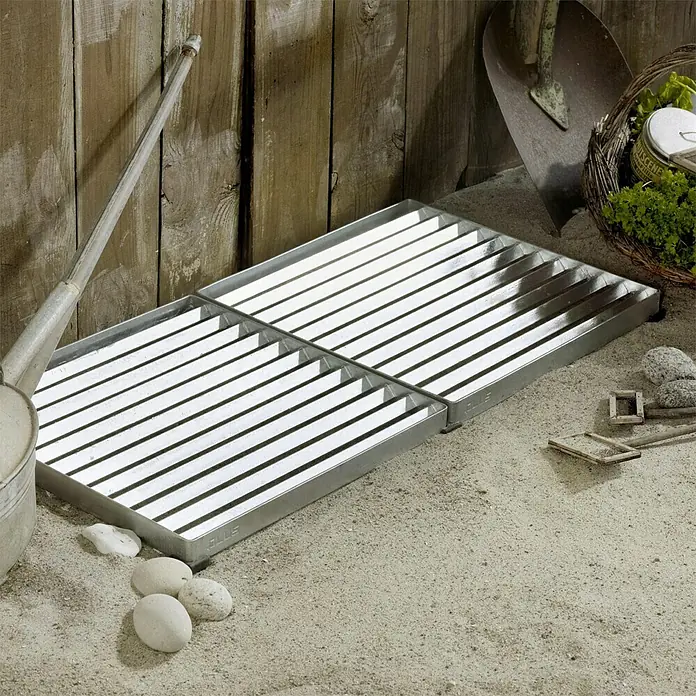 Plus Fußabtreter Cubic40 x 80 x 3,5 cm, Silber - Ansicht von vier quadratischen, feuerverzinkten Metallrosten auf sandigem Untergrund. Ideal als belastbarer und wetterfester Bodenbelag für den Außenbereich.