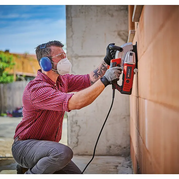 Einhell Rozadora TE-MA 1700 - 1.700 W, Diámetro disco: 150 mm - Un hombre está arrodillado cortando una ranura en una pared de ladrillos con una Einhell rozadora de pared, usando equipo de protección.