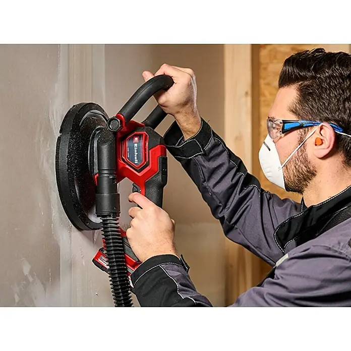 Einhell Professional PXC 18V Lijadora de paneles de yeso de batería TP-DWS 18/225 Li BL Solo - 18 V, Sin batería - Un hombre lijando una pared con una lijadora de paneles de yeso Einhell, que está conectada a una aspiradora.