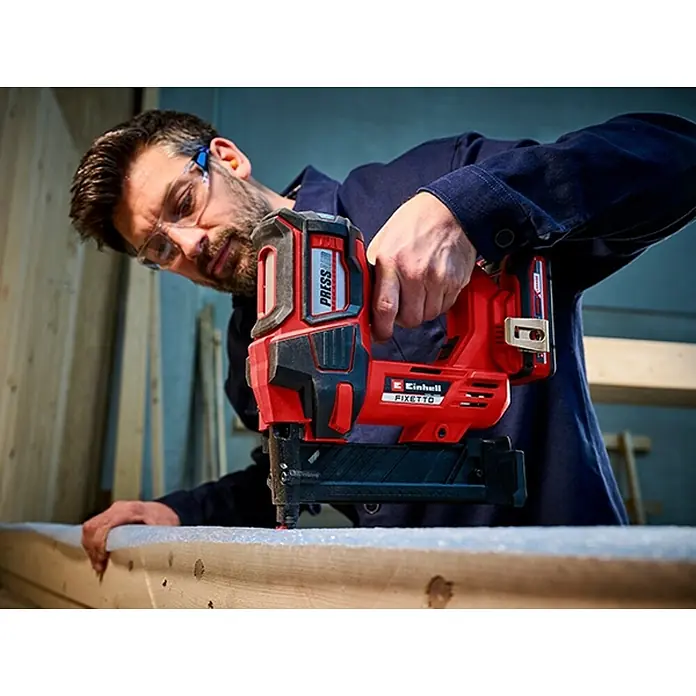 Einhell Professional PXC 18V Grapadora de batería FIXETTO 18/38 S - 18 V, Sin batería - Un hombre está usando una clavadora inalámbrica Einhell FIXETTO para sujetar madera. Lleva gafas de seguridad para la seguridad laboral.