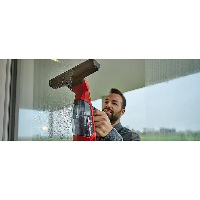 Einhell PXC 18V Limpiadora de cristales de batería Brillianto - 18 V, Sin batería, Volumen de recipiente: 0,1 l - Un hombre usa un limpiacristales inalámbrico Einhell para limpiar una ventana. El limpiacristales es rojo y negro con un recipiente transparente.