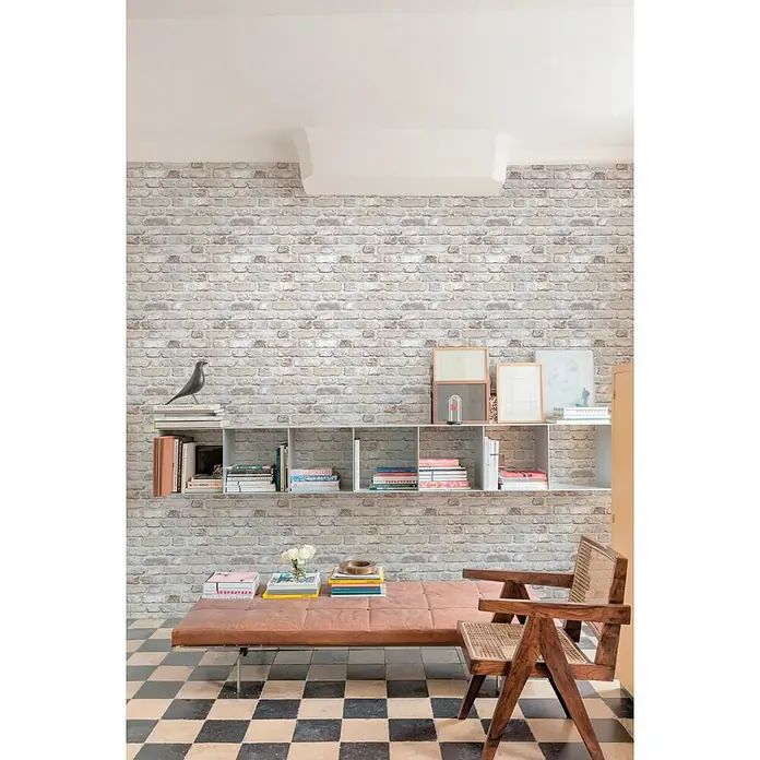Papel pintado Ladrillo - Gris, Efecto piedra, 10,05 x 0,53 m - Interior elegante con una estantería moderna, un sofá elegante y una silla de madera destacada contra una pared de ladrillo.
