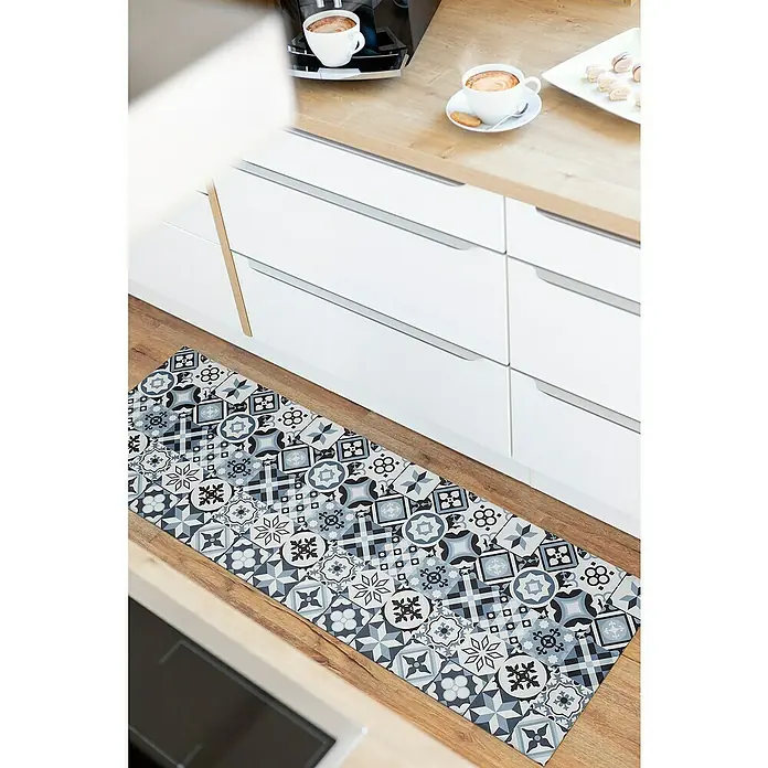 Teppichläufer MarrakeschGrau, 150 x 50 cm, 100 % Polyvinylchlorid - Nahaufnahme einer Küchenmatte mit marokkanischen Fliesenmustern auf einem Holzboden, die vor weißen Küchenschränken liegt.