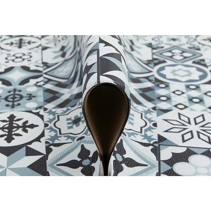 Teppichläufer Marrakesch - Grau, 150 x 50 cm, 100 % Polyvinylchlorid - Nahaufnahme einer dekorativen Bodenmatte mit einem blauen Fliesenmuster, die aufgerollt ist und ihre braune Unterseite zeigt.