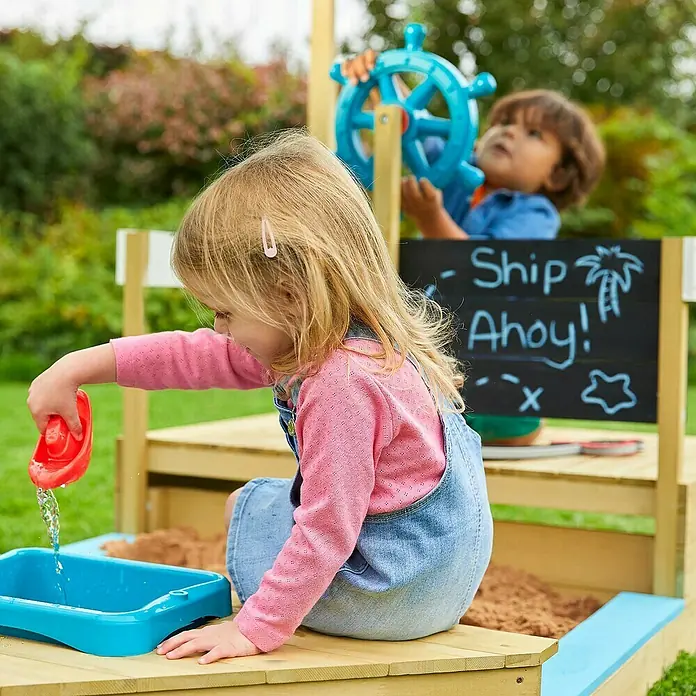 TP Toys Sandkasten Ahoy - 180 x 92 x 118 cm, Holz, Natur/Weiß, Blau - Eine Nahaufnahme eines Outdoor-Spielsets mit einem Sandkasten und einer Tafel, auf dem Kinder mit Wasser und Sand spielen.