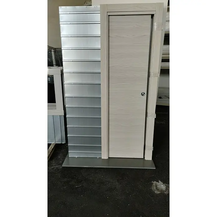Odem Estructura de puerta corredera para pared de placa de yeso laminado Único - 80 x 203 cm, Grosor 90 mm, Pared de yeso, Acero - Puerta de madera gris con marco junto a un armario de metal plateado. Un elemento interior moderno y elegante para tu hogar.