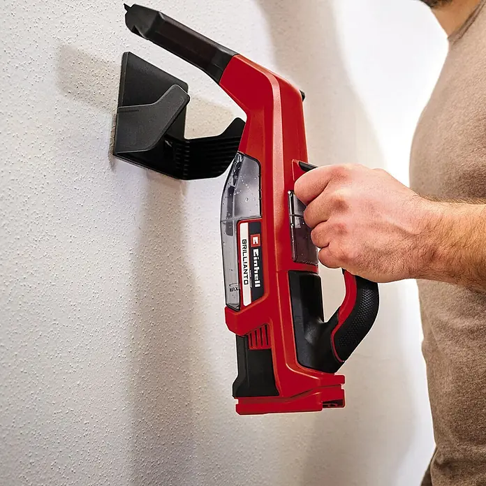 Einhell PXC 18V Limpiadora de cristales de batería Brillianto - 18 V, Sin batería, Volumen de recipiente: 0,1 l - La aspiradora de mano inalámbrica Einhell TE-VC 18 Li-solo, un dispositivo rojo, cuelga de un soporte de pared negro.