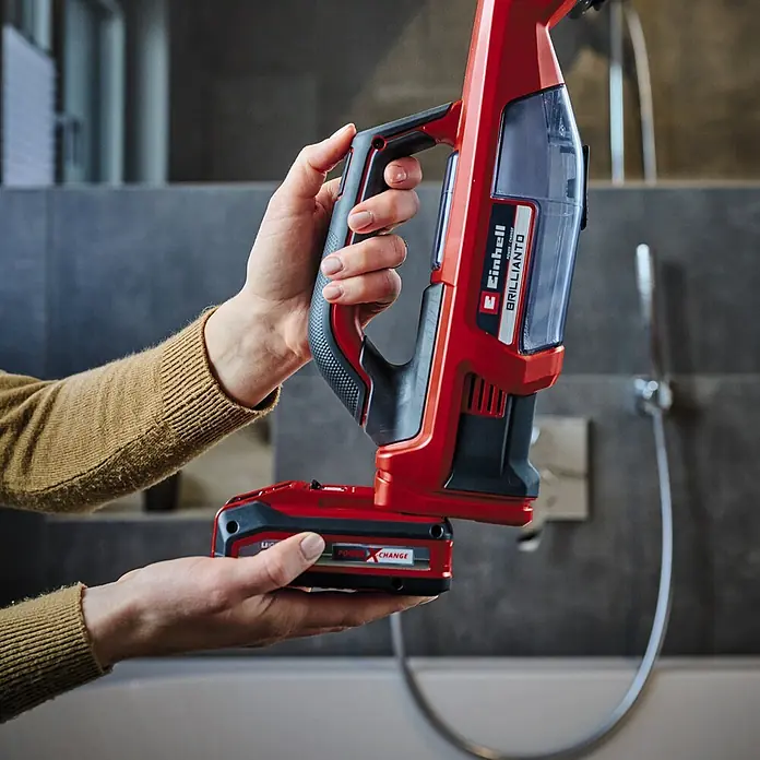 Einhell PXC 18V Limpiadora de cristales de batería Brillianto - 18 V, Sin batería, Volumen de recipiente: 0,1 l - Primer plano de la aspiradora inalámbrica Einhell Brillianto sujetada por manos. La aspiradora es roja y negra con un contenedor de polvo transparente.