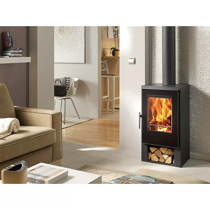 Panadero Kaminofen Andes - 7,5 kW, Raumheizvermögen: 230 m³, Schwarz Metallic - Schwarzer freistehender Kaminofen mit Glastür, der Flammen und ein integriertes Holzfach darunter zeigt, in einem modernen Wohnzimmer.