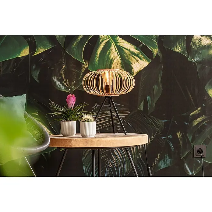 Komar Pure Fototapete Tropical Wall - 3 -tlg., B x H: 400 x 250 cm, Vlies - Tischleuchte mit Drahtschirm und drei Beinen, die ein warmes und einladendes Licht verbreitet, auf einem Holztisch mit Pflanzen.
