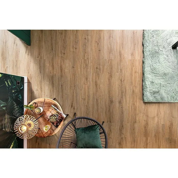 b!design Vinylboden Rigid Maxi - Ashton Eiche, Landhausdiele, 1.220 x 228 x 4,8 mm - Nahaufnahme eines gemütlichen Wohnbereichs mit einem attraktiven Holzboden, einem Teppich, einem Holztisch und einem Rattansessel.