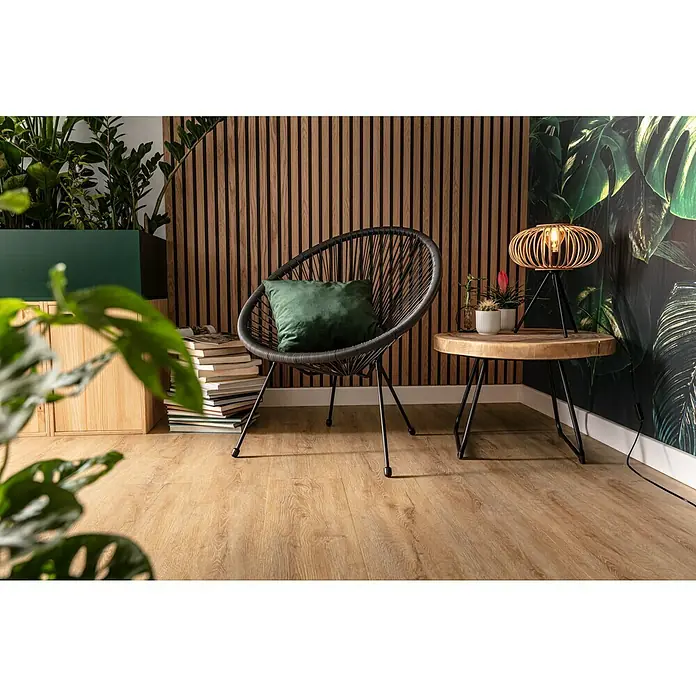 b!design Vinylboden Rigid Maxi - Ashton Eiche, Landhausdiele, 1.220 x 228 x 4,8 mm - Gemütlicher Lesebereich mit einem stilvollen Rattansessel und einem kleinen Beistelltisch, der mit einer Lampe dekoriert ist.