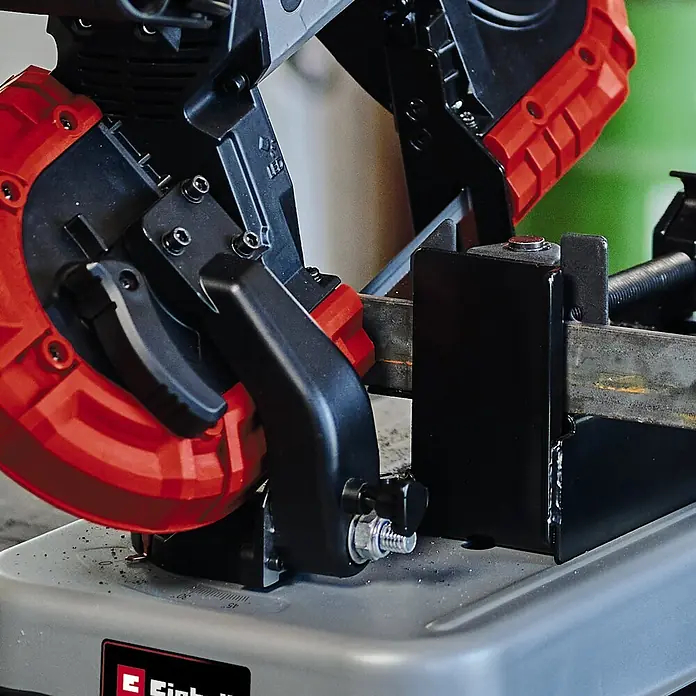 Einhell PXC 18V Sierra de cinta de batería TE-MB 18/127 Li-Solo - 18 V, Sin batería - Primer plano de una sierra de metal cortando una pieza de metal, destacando el esquema de colores rojo y negro de la herramienta.
