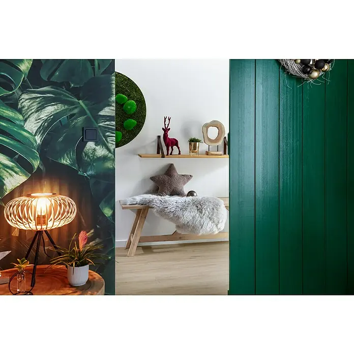 Alpina Wandfarbe Feine Farben - Tochter der Antike, Matt, 2,5 l, Konservierungsmittelfrei - Dekoratives Interieur mit tropischen Blättern, einer Lampe mit Käfigdesign, einer Mooswand, einem Holzregal und einem smaragdgrünen Holzpaneel.