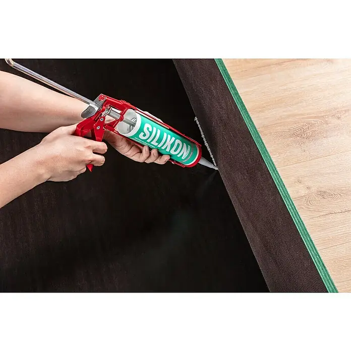Sanitär-Silikon - Grau, 300 ml - Eine Person trägt Silikon mit einer Kartuschenpistole auf eine Oberfläche auf. Die grüne Silikonkartusche und die rote Kartuschenpistole sind gut sichtbar.