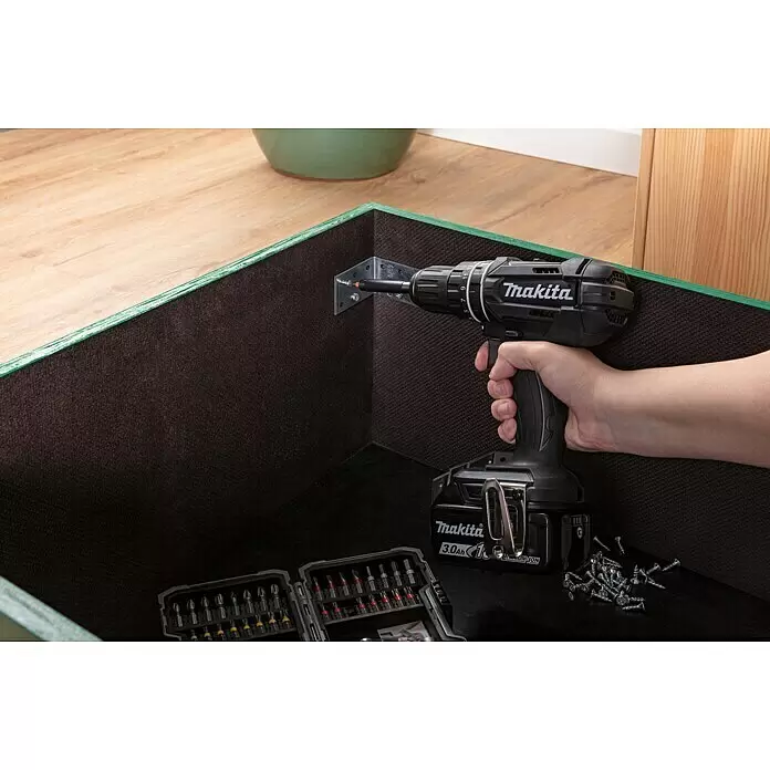 Makita LXT 18V Taladro atornillador de batería DDF482RFJ - 18 V, 2 baterías, 3 Ah, 62 Nm - Una mano utiliza un taladro inalámbrico Makita negro para fijar un soporte metálico dentro de una caja de madera marrón oscuro con bordes verdes.