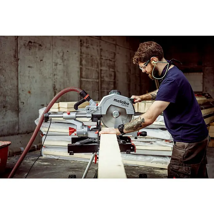 Metabo Kapp- & Gehrungssäge KGS 305 M - 1.600 W, Durchmesser Sägeblatt: 305 mm, Leerlaufdrehzahl: 3.700 U/min - Ein Handwerker benutzt eine Metabo Kappsäge KGS 305 M, um Holz zu schneiden. Die Säge steht im Fokus, während der Mann im Hintergrund arbeitet.