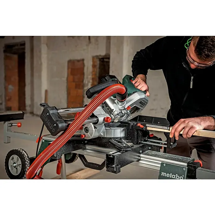 Metabo Kapp- & Gehrungssäge KGS 216 M Set - 1.500 W, Durchmesser Sägeblatt: 216 mm, Leerlaufdrehzahl: 5.000 U/min - Eine Metabo Kapp- und Gehrungssäge im Einsatz, mit rotem Absaugschlauch, die Holz präzise zuschneidet. Ideal für den professionellen Handwerker.