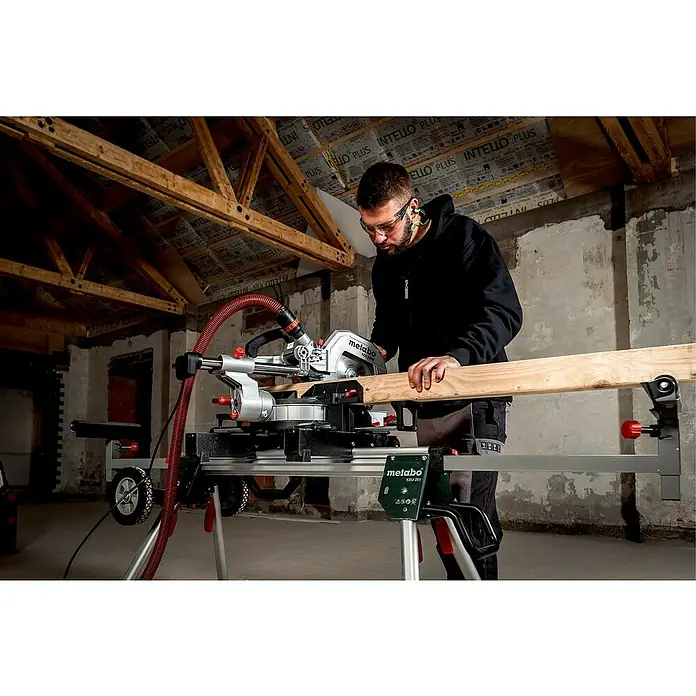 Metabo Kapp- & Gehrungssäge KGS 216 M Set - 1.500 W, Durchmesser Sägeblatt: 216 mm, Leerlaufdrehzahl: 5.000 U/min - Ein Mann benutzt eine Metabo KSU 251 Kapp- und Gehrungssäge mit Tisch, um ein Holzbrett zu schneiden. Schutzbrille und Gehörschutz werden getragen.