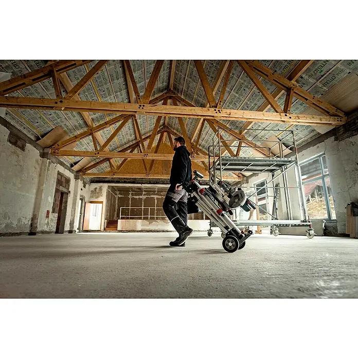 Metabo Kapp- & Gehrungssäge KGS 216 M Set - 1.500 W, Durchmesser Sägeblatt: 216 mm, Leerlaufdrehzahl: 5.000 U/min - Ein Handwerker transportiert eine Metabo Kapp- und Gehrungssäge auf einem Metabo Transportwagen in einem Rohbau.