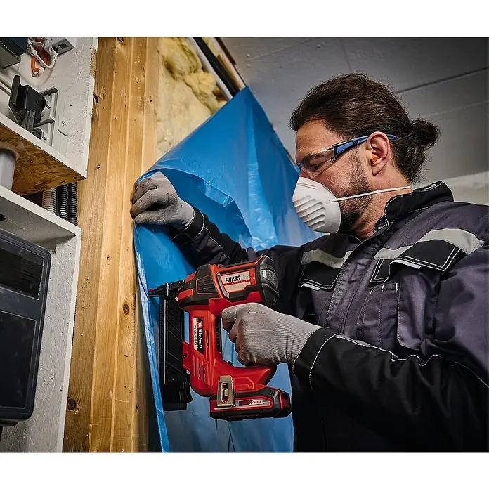 Einhell Professional PXC 18V Grapadora de batería FIXETTO 18/38 S - 18 V, Sin batería - Un hombre fija láminas de plástico azul a una pared de madera con una grapadora inalámbrica Einhell y equipo de protección.