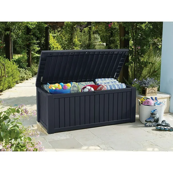 Keter Gartenbox Rockwood - 570 l, Kunststoff - Eine dunkelblaue Gartenbox mit geöffnetem Deckel, gefüllt mit Spielzeug und Kissen, steht im Freien auf einer Terrasse.