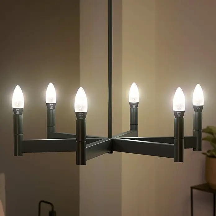 Philips Hue LED-Lampe Filament Classic White Ambiance - E14, 350 lm, Einstellbare Farbtemperatur, 1 Stk. - Elegante Nahaufnahme eines schwarzen Kronleuchters mit sechs Philips Hue Kerzenlampen, die warmes Licht spenden und eine gemütliche Atmosphäre schaffen.