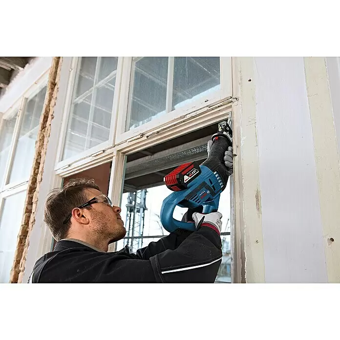 Bosch Professional AMPShare 18V Sierra de sable de batería GSA 18V-32 - 18 V, Sin batería, 0 /min - 2.500 /min, Maleta - Hombre con gafas de seguridad usa una sierra de sable sin cable Bosch azul y negra con batería de 18V para cortar un marco de ventana.
