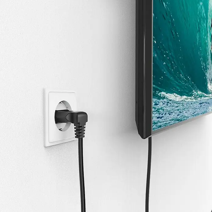 Hama Netzkabel 90° gewinkelt Doppelnut C7 - Weiß/Schwarz, Länge: 1,5 m, Eurostecker, 2,5 A - Nahaufnahme eines an eine weiße Wand angeschlossenen Fernsehers mit einem Winkelstecker in einer Steckdose.