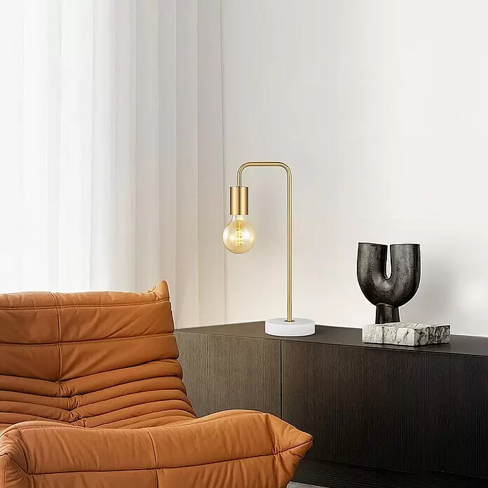 Deko-Tischleuchte Noble - 10 W, L x B x H: 20,3 x 40 x 20,3 cm, Gold - Goldene Tischleuchte mit Edison-Glühbirne und weißem Fuß, auf einem dunklen Schrank platziert.