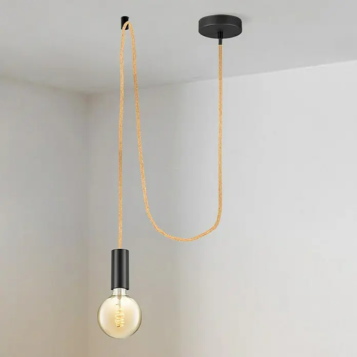 Home Sweet Home Lampenpendel FabricNatur, 215 mm, E27 - Eine einzelne Glühbirne hängt an einem schwarzen Zylinder mit einem geflochtenen Kabel von der Decke. Das Kabel ist an einer Wand befestigt.