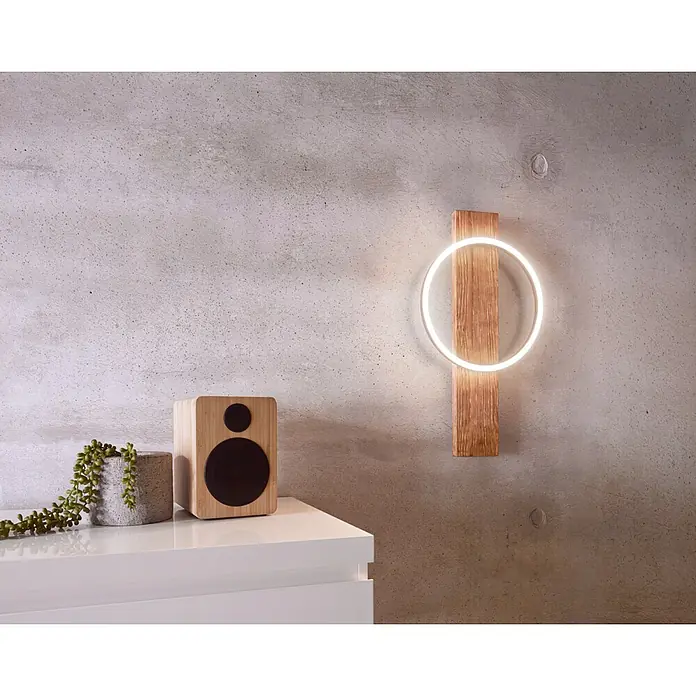 Eglo Boyal Aplique de pared LED - 12 W, Madera/Claro, Blanco cálido - Primer plano de una lámpara de pared LED redonda con base de madera, junto a un altavoz y una planta suculenta en un estante blanco.