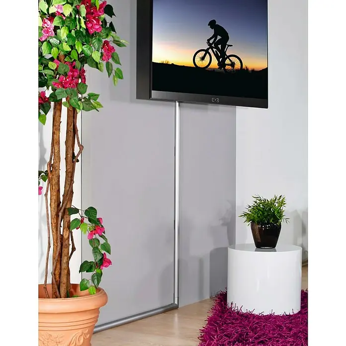 Hama Kabelkanal - 1,1 m x 33 mm x 18 mm, Aluminium - Ein an der Wand montierter Fernseher zeigt das Bild eines Radfahrers im Gegenlicht bei Sonnenuntergang. Dekoratives Grün und eine Rohrverkleidung ergänzen das Setup.