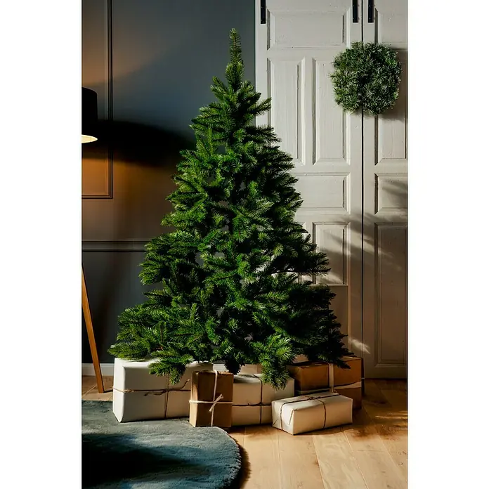 Künstlicher Weihnachtsbaum Canada Spruce - Höhe: 180 cm, Grün, Standfuß - Dekoriert mit dezenten Geschenken präsentiert sich ein grüner Weihnachtsbaum vor einer grauen Wand und einer verzierten Tür.