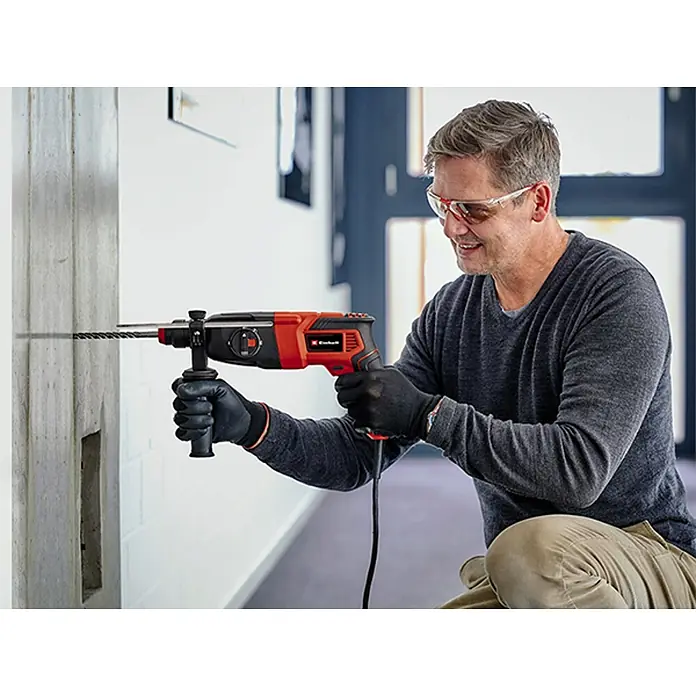 Einhell Martillo combinado TC-RH 620 4F Kit - 620 W, 2,2 J, Alojamiento SDS-Plus - Un hombre perforando una pared con un martillo perforador Einhell, con gafas de seguridad y guantes.