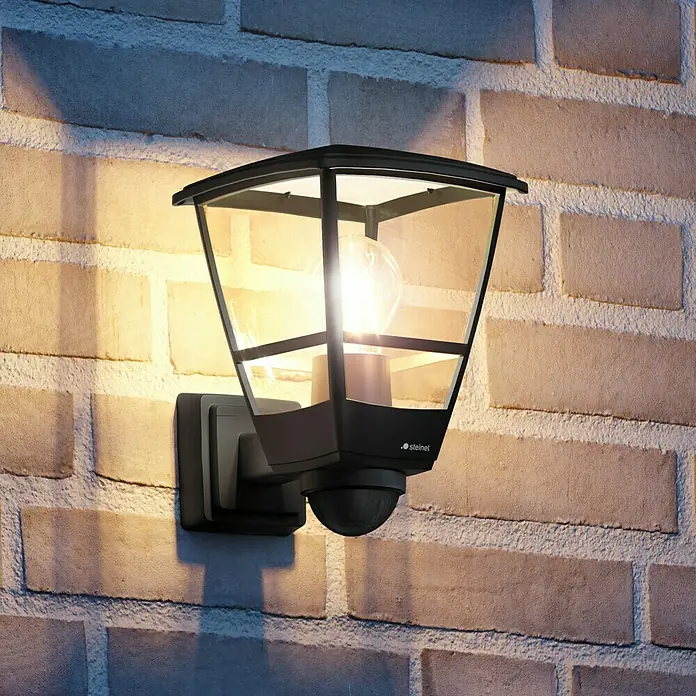 Steinel Aplique exterior L 10 SSW - 15 W, 22,4 x 17,5 x 25,5 cm, Negro, IP44, Con sensor de movimiento - Una moderna lámpara de exterior Steinel con sensor de movimiento montada en una pared de ladrillo.